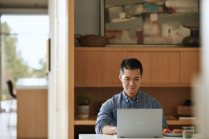 Adult male mobile professional on the go with ASUS ZenBook. Working at kitchen table with glass of water.