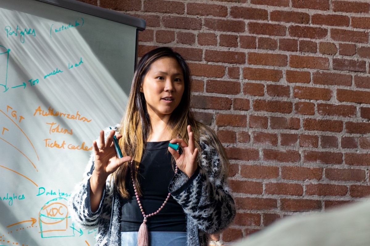 Female developer speaking in front of a white board during team stand up meeting.