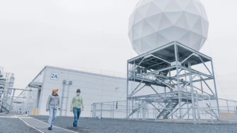 Photo of Orbital Ground Station satellite uplink. Two male datacenter employees walk side by side beneath the orbital ground station