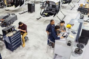 Overhead view of three first line workers on helicopter factory floor at commercial manufacturing plant.