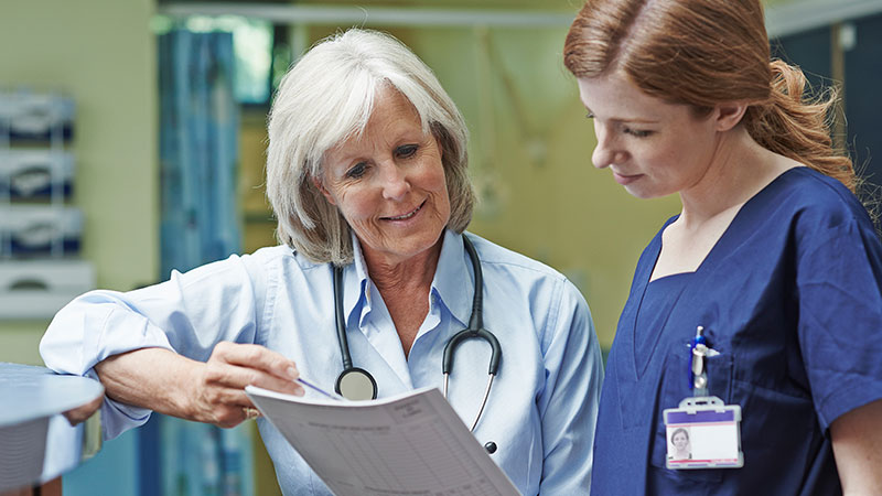 A smiling doctor looks at a report alongside a nurse