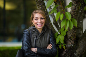 Mina Aitelhadj poses for a photo outside of her Microsoft building. She’s leaning up against a tree trunk.