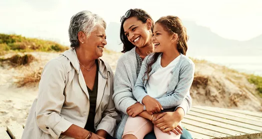 Grandmother, mother and daughter smiling and laughing on a beach