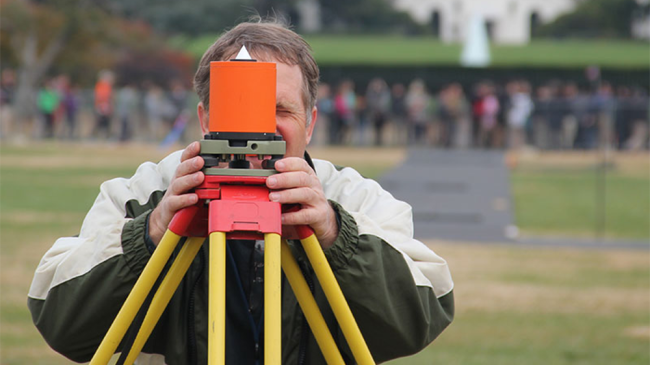 A geodesist on the National Mall looks through a surveying device.