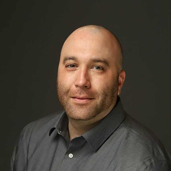 A bald man in a gray shirt is posing for a photo.