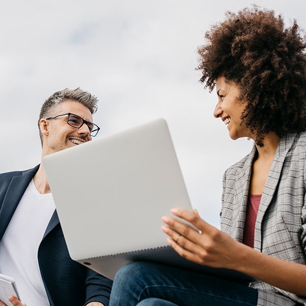 Two business people sitting on a bench looking at a laptop.