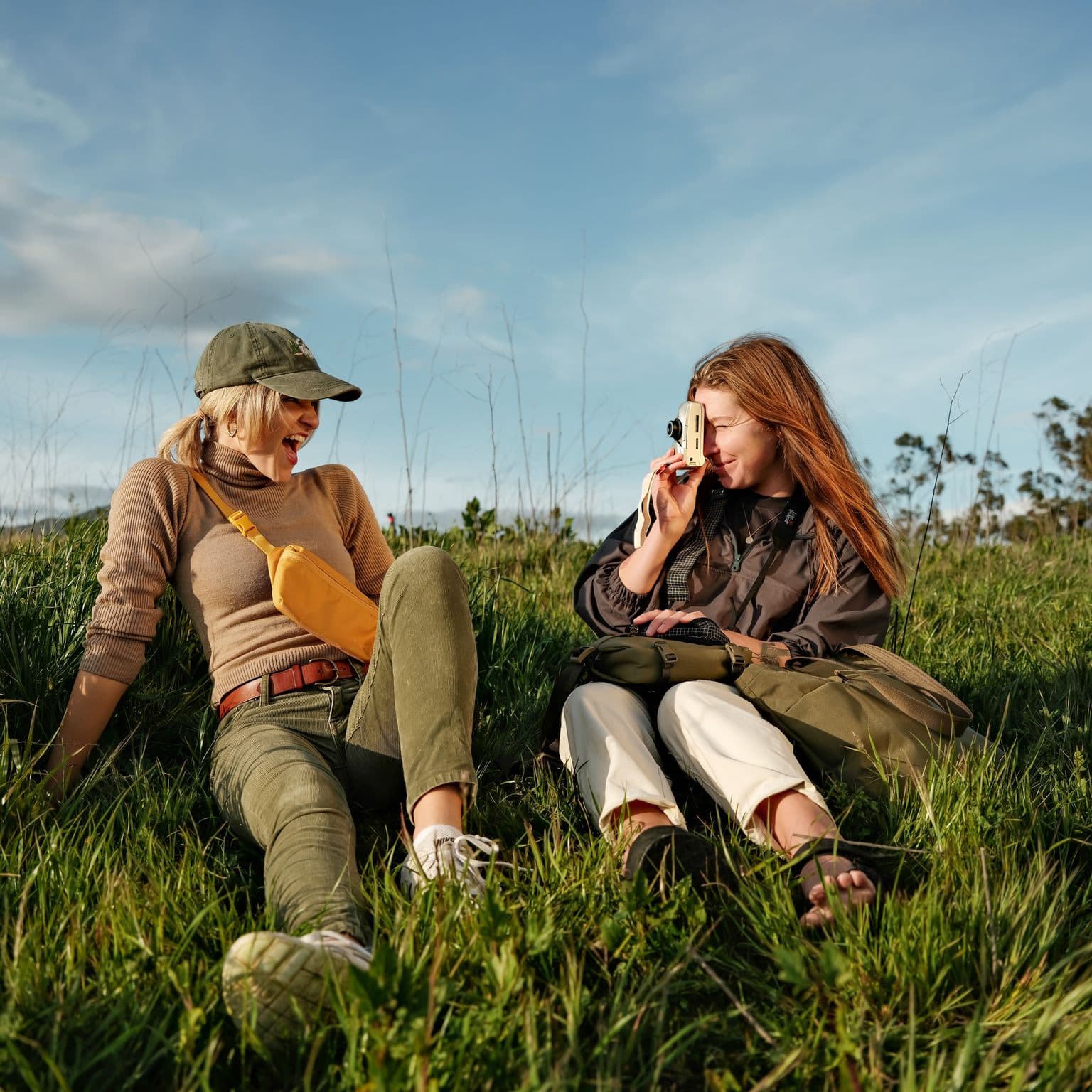 Two girls laughing and taking pictures in a field with Moment Bags.