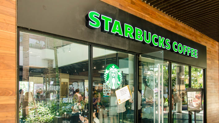 A starbucks coffee shop with people walking in front of it.