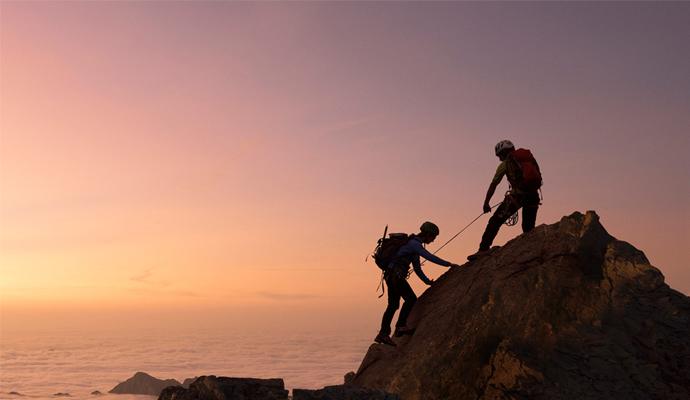 Photograph of two people in climbing gear reaching a mountain peak