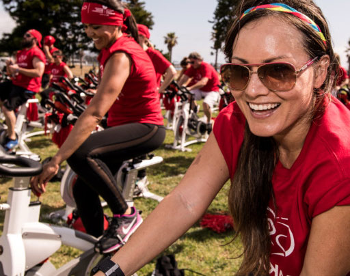 a group of people in red t-shirts riding stationary bikes in a park setting