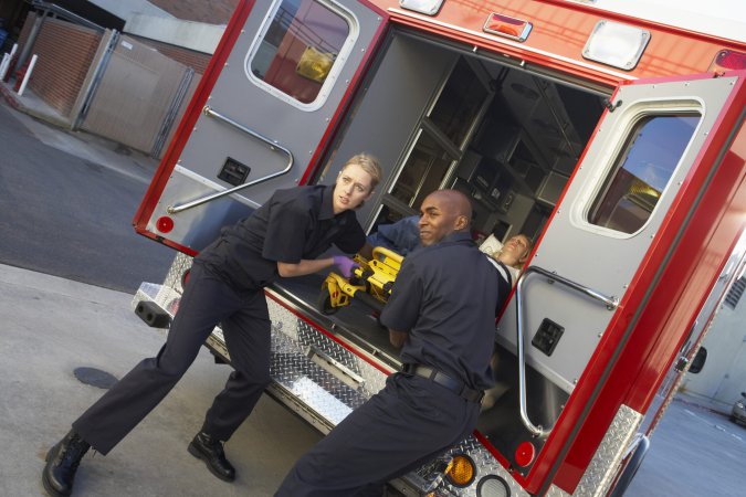 two paramedics prepare to take someone out of an ambulance 