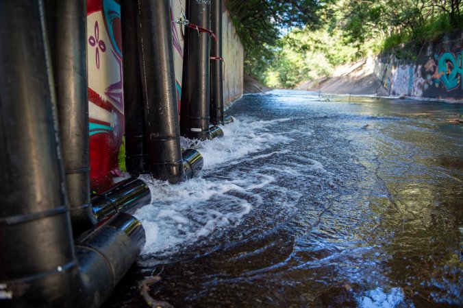 Well water from Red Hill Navy fuel facility being pumped out through pipes into the Halawa Stream surrounded by pink and white graffiti