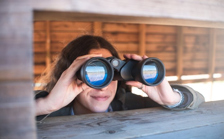 Kids with long frizzy brown hair birdwatching with binoculars from a duck blind