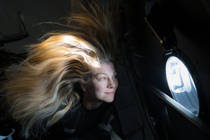 a woman with blonde hair that floats near a window overlooking earth from above