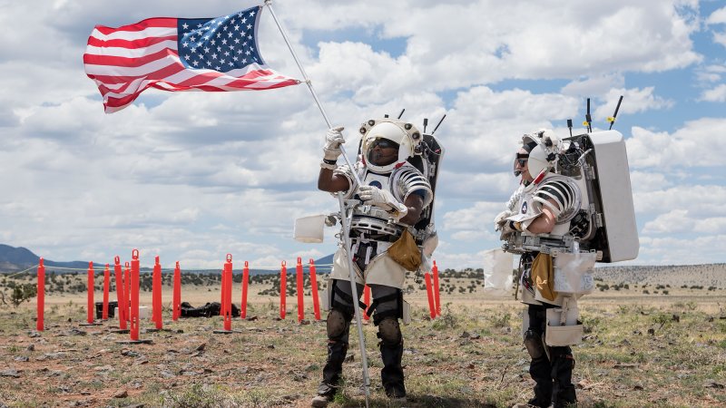 NASA astronaut Andre Douglas raises an American flag as NASA astronaut Kate Rubins looks on during their first simulated moonwalk in a week-long field test consisting of four simulated moonwalks and six advanced technology runs in the San Francisco Volcanic Field in Northern Arizona on May 13, 202