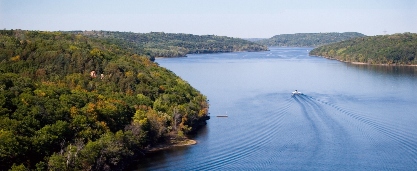 Aerial shot of a wide river with a boat traveling up the middle leaving a wake.