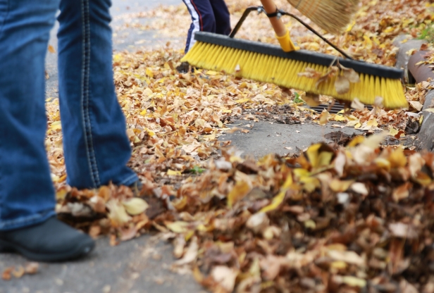 Feet and legs of a person sweeping piles of leaves away from a storm drain.