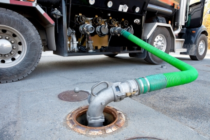 Fuel delivery tanker truck filling up underground gas storage tank.