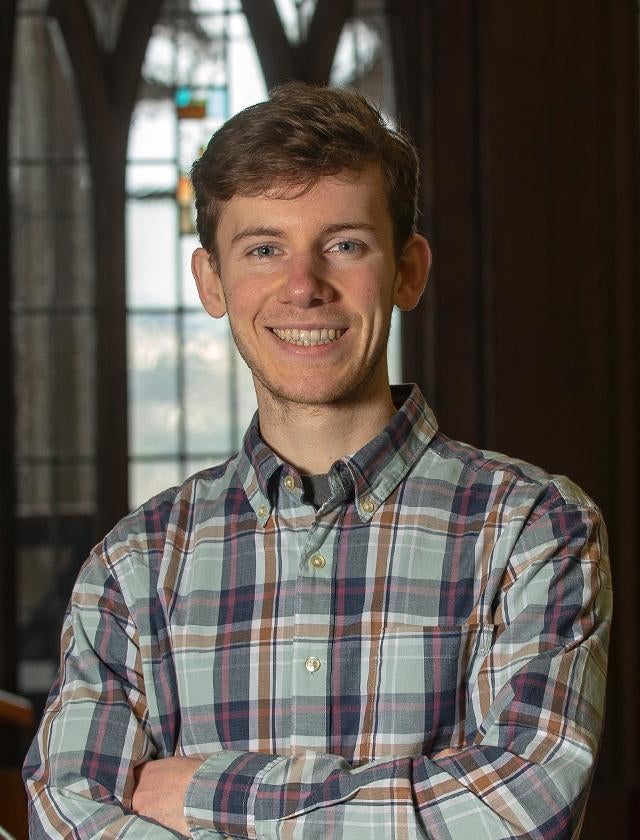 Asher Hancock smiling in plaid shirt with arms folded