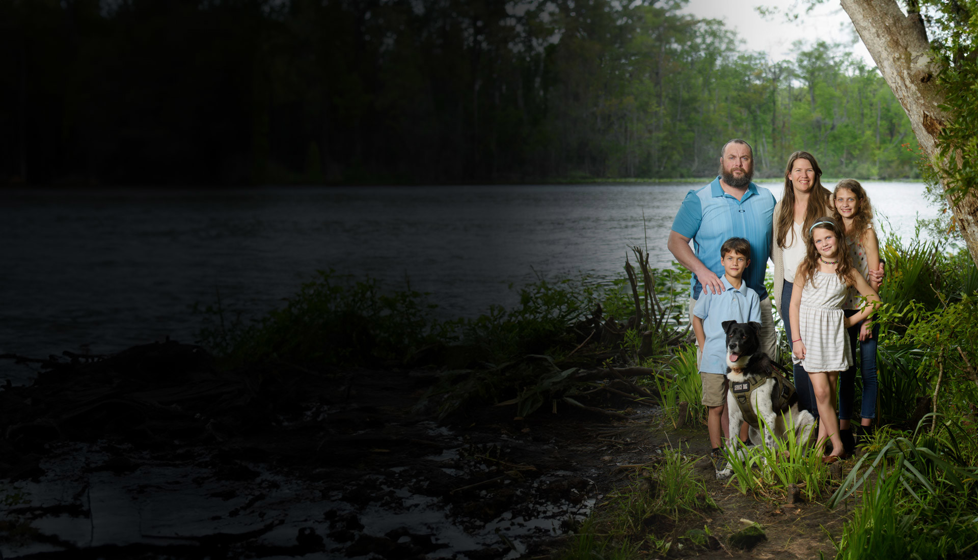 Family support member and caregiver, Jenna Malone, her husband Issac and their children stand next to tree smiling at camera.