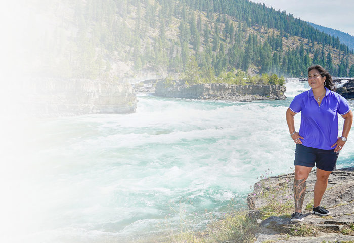 Wounded Warrior Tina Waggener stands in front of a tree-covered mountain and river while gazing at the scenery.