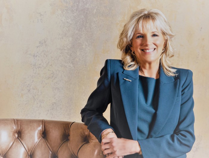 Dr. Jill Biden wears a blue suit, standing next to leather armchair