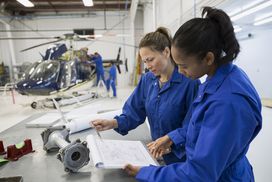 Airplane mechanics looking at paperwork and working on a helicopter