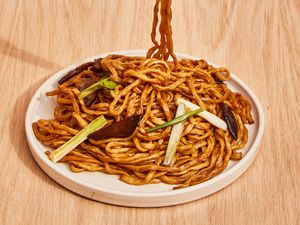 A plate loaded up with longevity noodles, showing mushrooms and scallions mingled with the glazed noodles