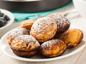 Plate of aebleskiver with powdered sugar on top and a side of blueberries next to the plate.