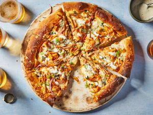 A buffalo chicken pizza cut into slices, served with glasses of beer