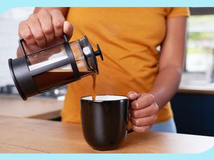 Someone pouring coffee from a French press into a black coffee mug