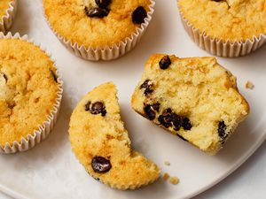 A close-up of a plate with chocolate chip muffins on it, with one of the muffins shown broken in half to reveal the tender interior