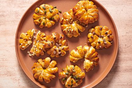 A large orange plate with caramel apple puff pastry doughnuts, garnished with pepitas, chocolate chips, and crushed pretzels