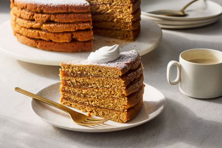 A slice of Appalachian apple stack cake, topped with whipped cream and served with a mug of coffee