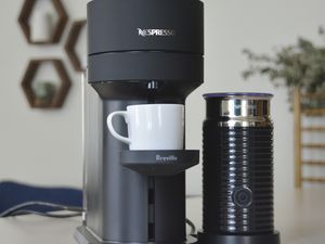 Nespresso Vertuo Next displayed on a grey surface with wooden frames hanging on the wall behind it