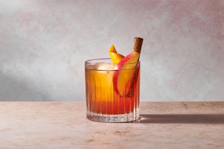 An apple cider old fashioned cocktail, garnished with a slice of apple, an orange peel, and a cinnamon stick