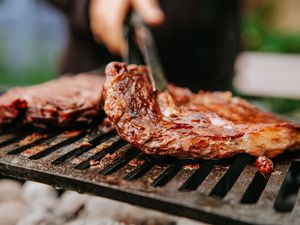 Woman doing BBQ Steaks on a flame grill.