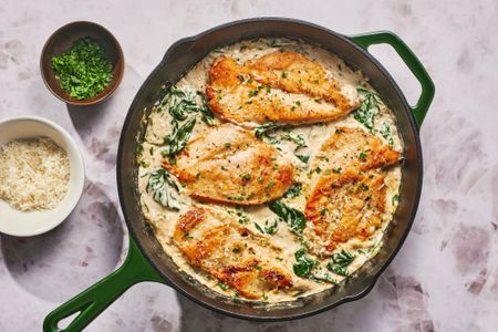 A skillet of chicken Florentine with extra parsley and parmesan cheese served on the side