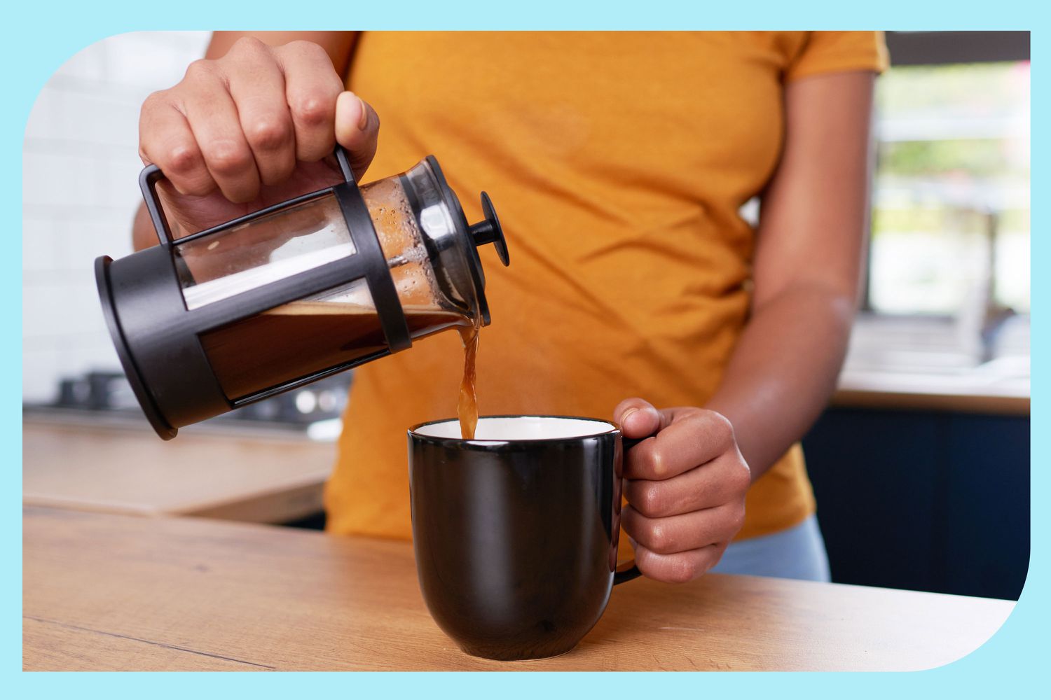 Someone pouring coffee from a French press into a black coffee mug