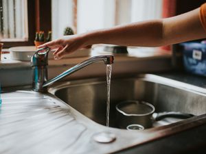 A hand reaching out to turn off the faucet with running water.