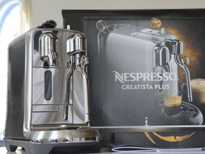 Nespresso Creatista Plus Espresso Machine displayed on a white counter next to its retail box and guide