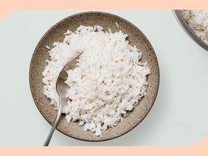 An earthenware bowl filled with white rice with a serving spoon sticking out