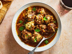 A bowl of French onion slow cooker meatballs topped with melted cheese and chopped parsley, and served with sliced bread and red wine