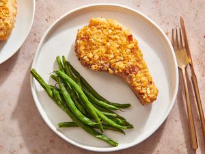 A plate with a shake 'n bake style pork chop and steamed green beans, with another plate in frame