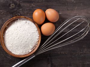 Whisk next to three eggs and a bowl of flour