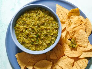 A bowl of tomatillo salsa served on a platter of tortilla chips