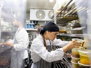 Two chefs looking at stainless steel shelves containing rows of containers full of wet ingredients 