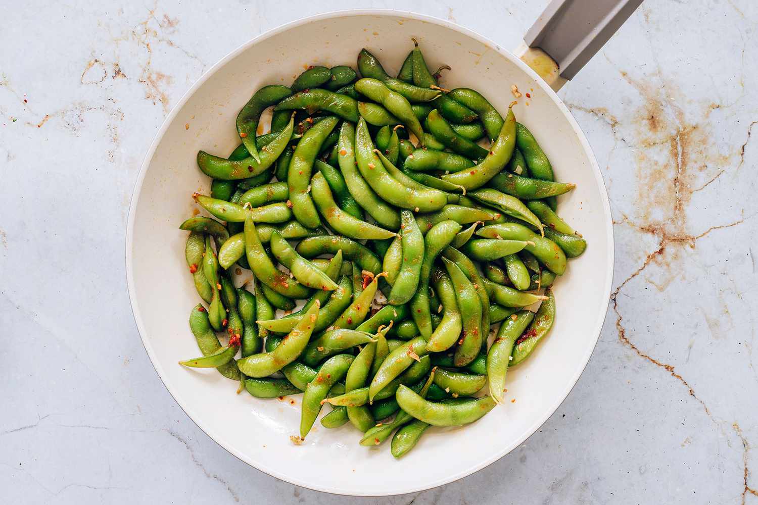 edamame in a pan with the garlic mixture and chili oil