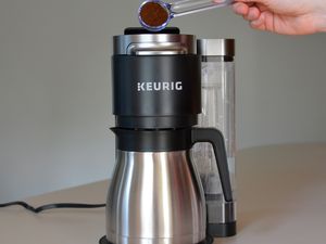 Hand emptying a spoonful of ground coffee into the Keurig K-Duo Plus Single Serve & Carafe Coffee Maker