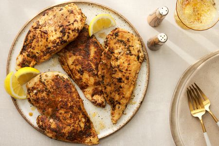 A plate of blackened chicken served with lemon wedges